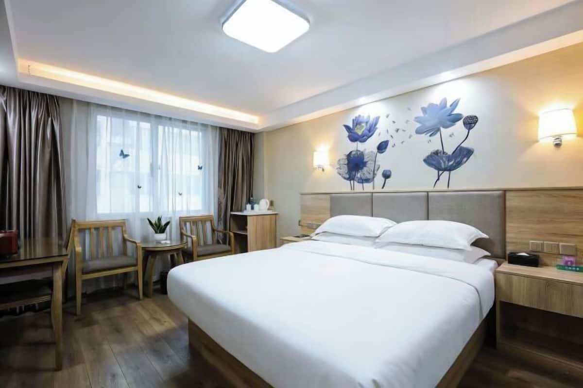 Une chambre d’hôtel avec un grand lit, un bureau, une chaise, une petite table et une lampe fixée au mur.