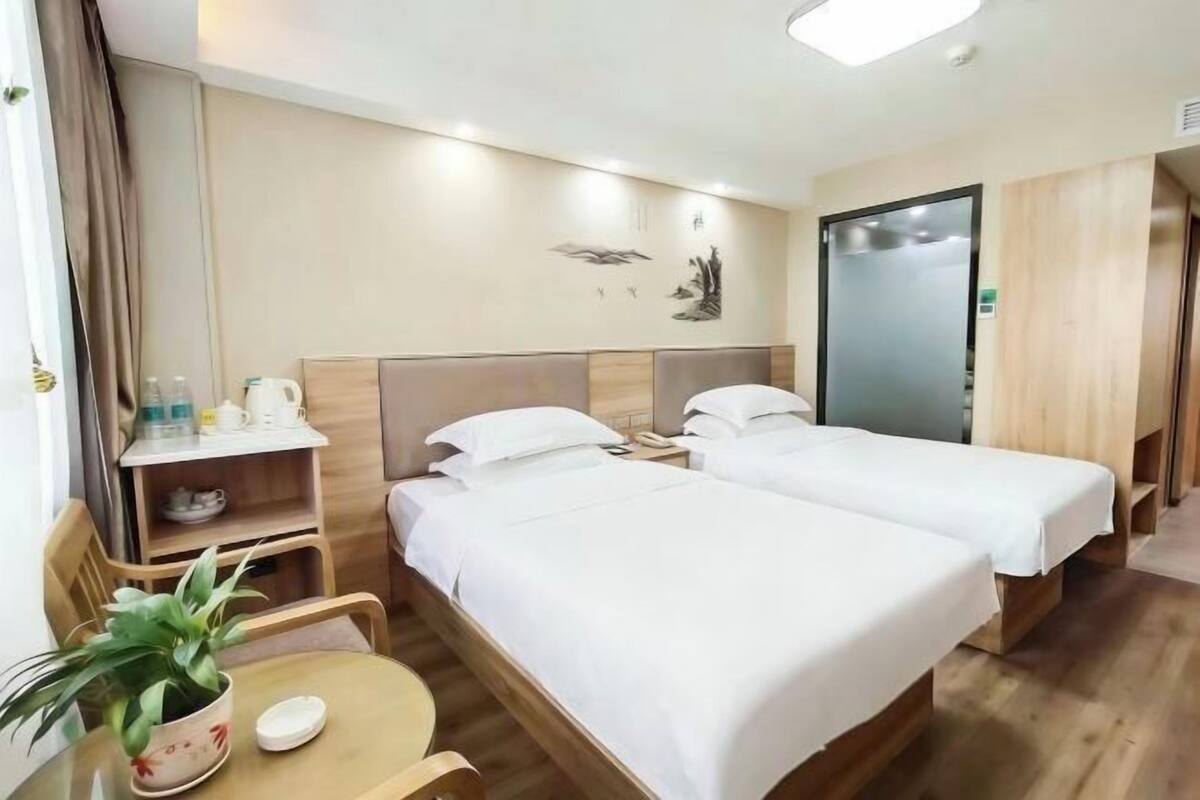 Une chambre d’hôtel avec deux lits, une petite table avec une plante, un miroir et une étagère avec des articles de toilette.