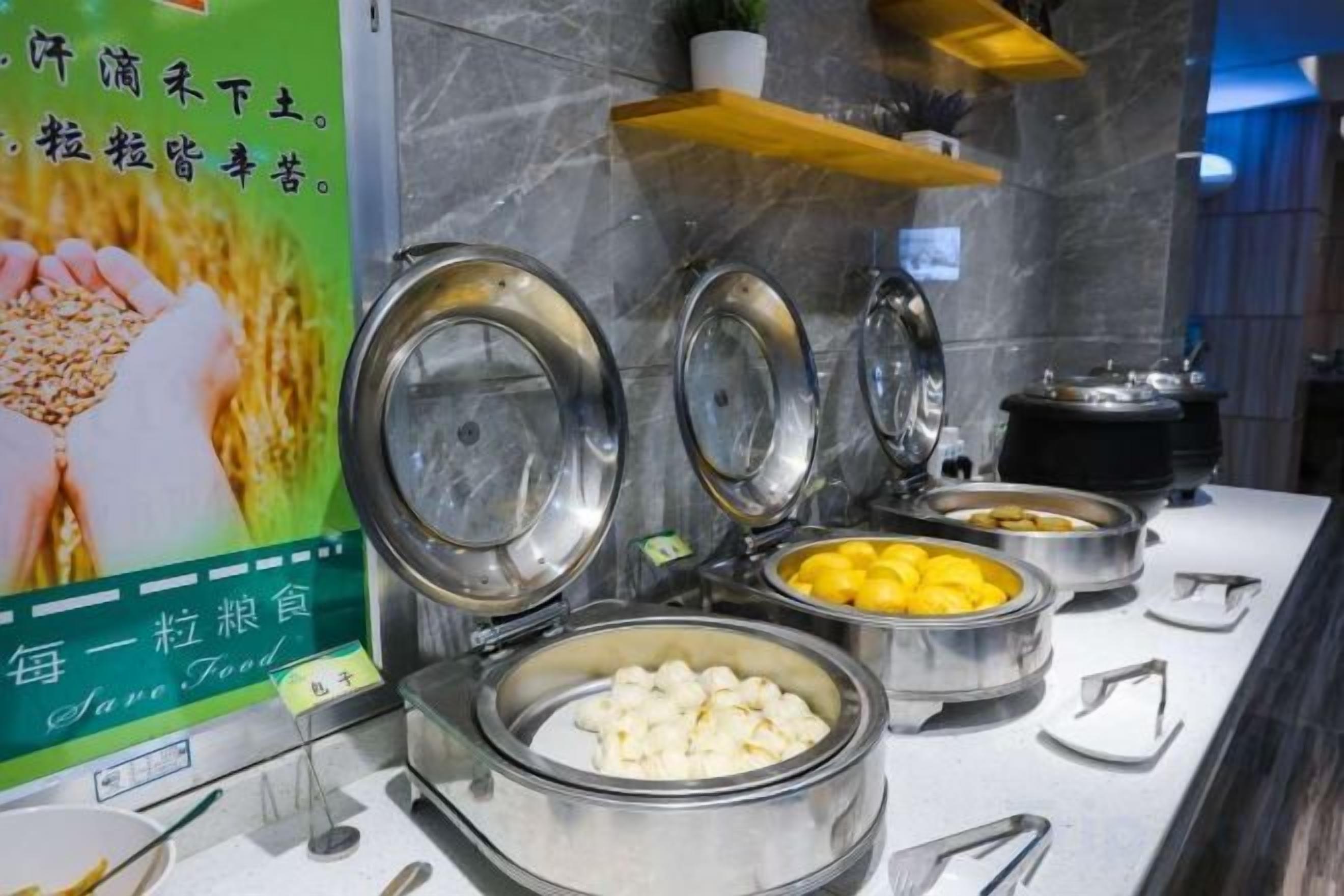 A buffet with various food items in metal containers, a sign with text, and a marble wall in the background.