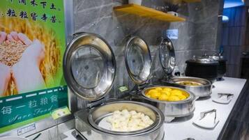 A buffet with various food items in metal containers, a sign with text, and a marble wall in the background.