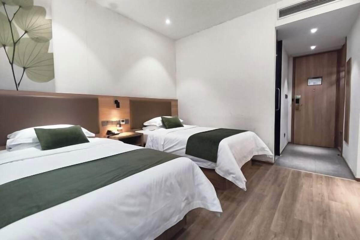 A hotel room with two beds, a wooden headboard, a nightstand, a wall-mounted lamp, and a door leading to another room.