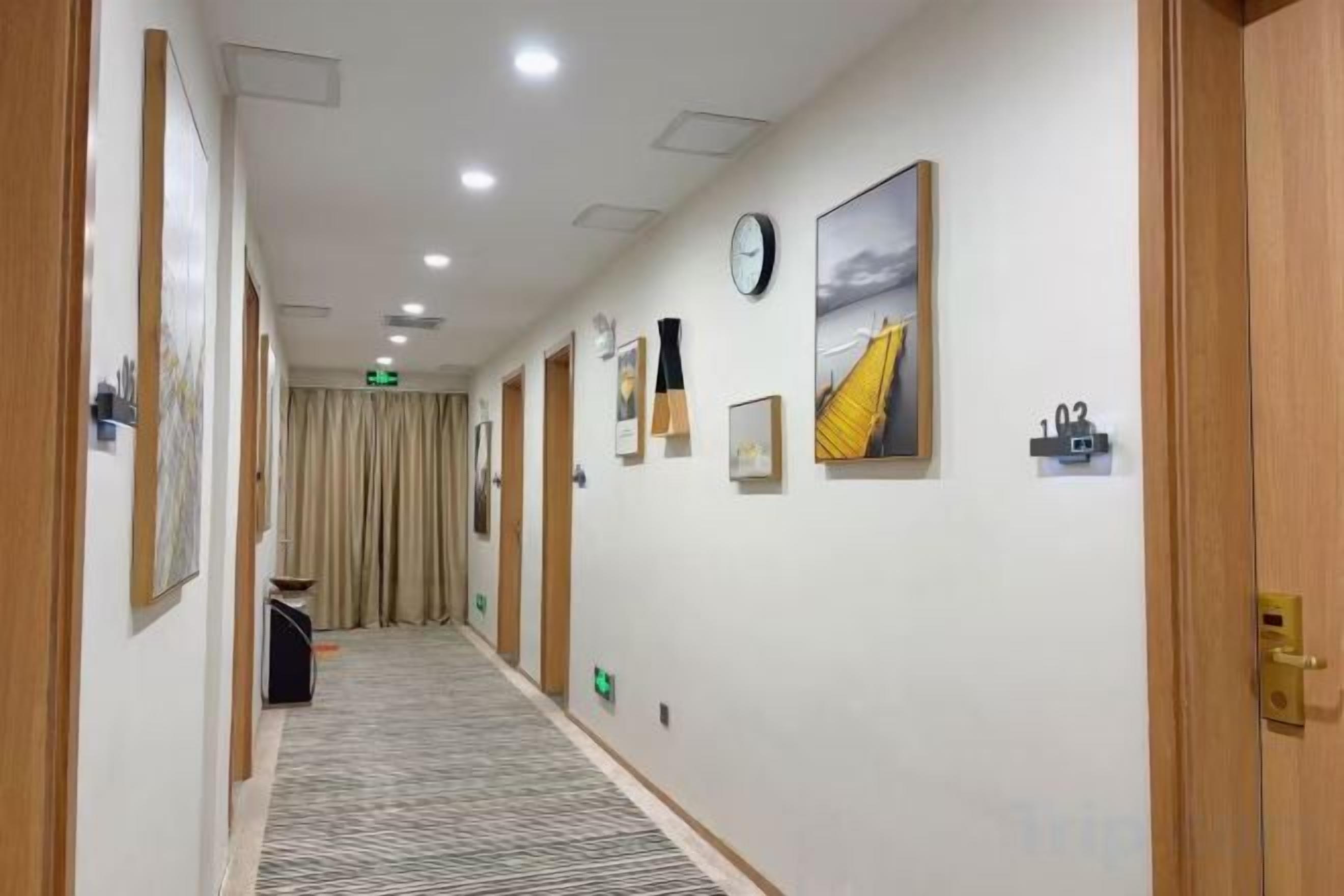 A hotel corridor with framed pictures on the walls, a clock, and a number sign.