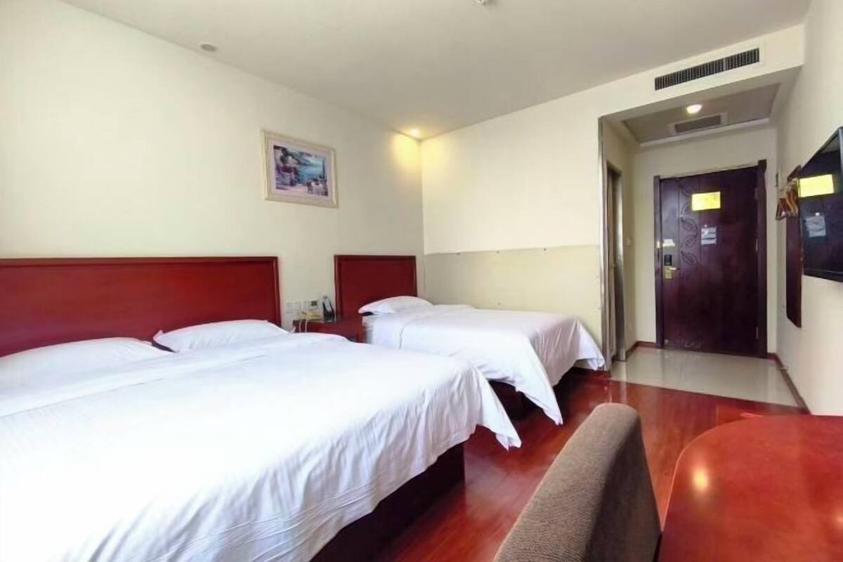 A hotel room with two beds, a wooden floor, a red headboard, a painting on the wall, and a door with a sign.