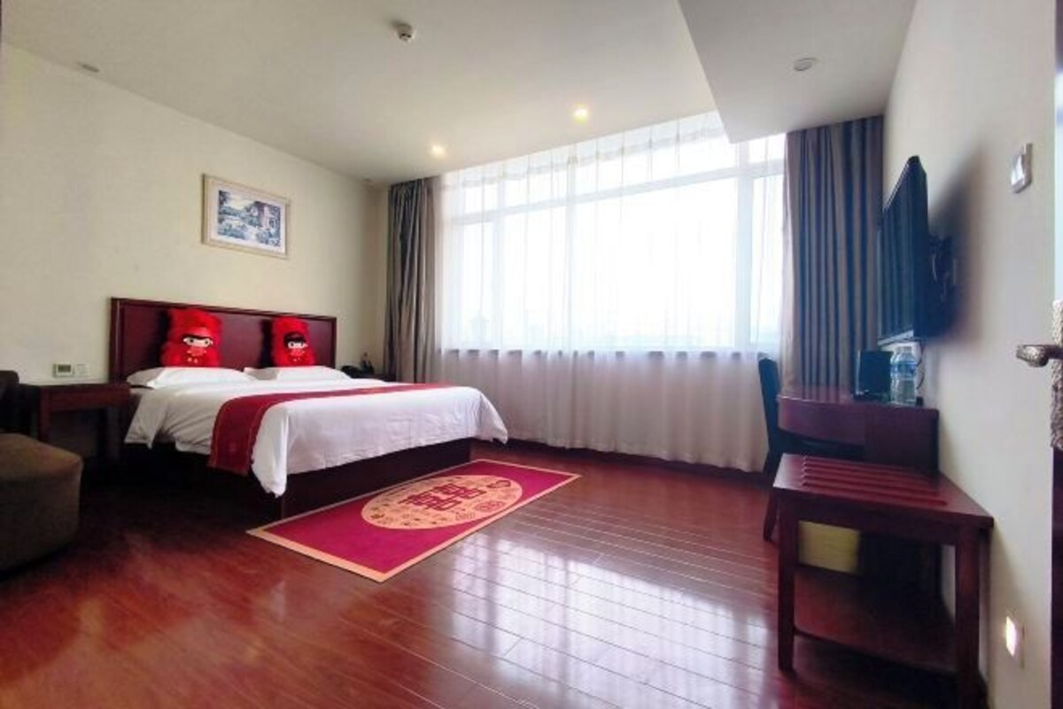 A hotel room with a bed, a desk, a chair, a TV, and a window with curtains.