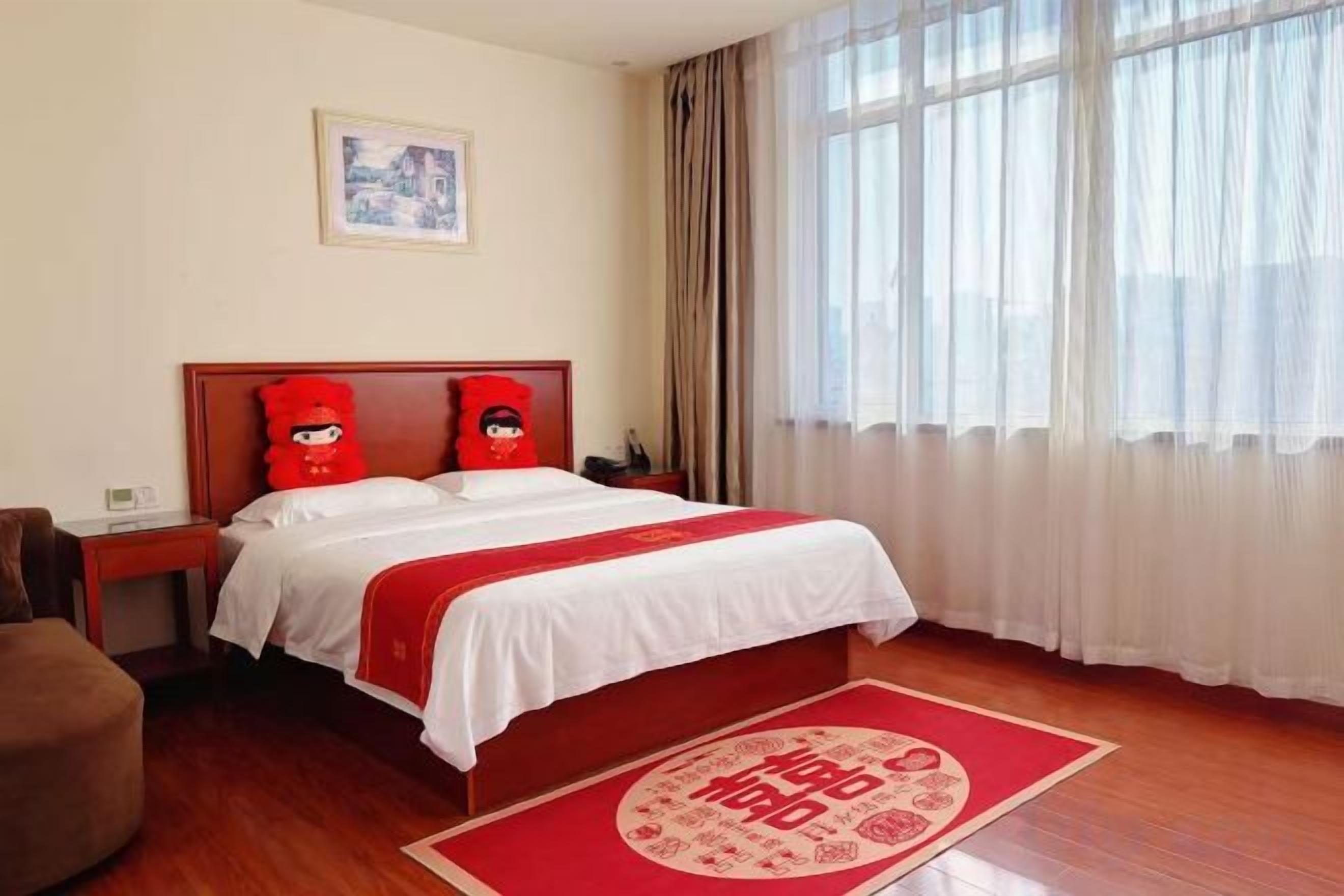 Een hotelkamer met een bed, nachtkastje, stoel en een raam met gordijnen.