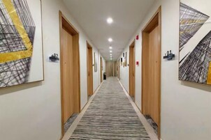 Un pasillo de hotel con puertas numeradas del 01 al 03, pisos alfombrados y obras de arte en las paredes.
