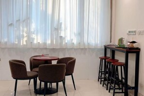 A dining area with a round table and four chairs, a bar counter with stools, and a window with sheer curtains. - GreenTree Liaocheng Yanggu Huangshan Road Shizilou (Yanggu)