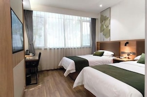 A hotel room with two beds, a desk, a chair, a window with curtains, and a wall-mounted lamp.