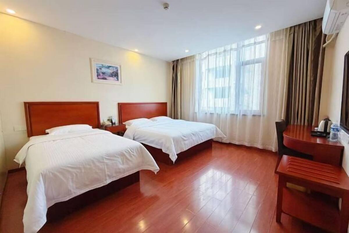 A hotel room with two beds, a desk, and a window with curtains.