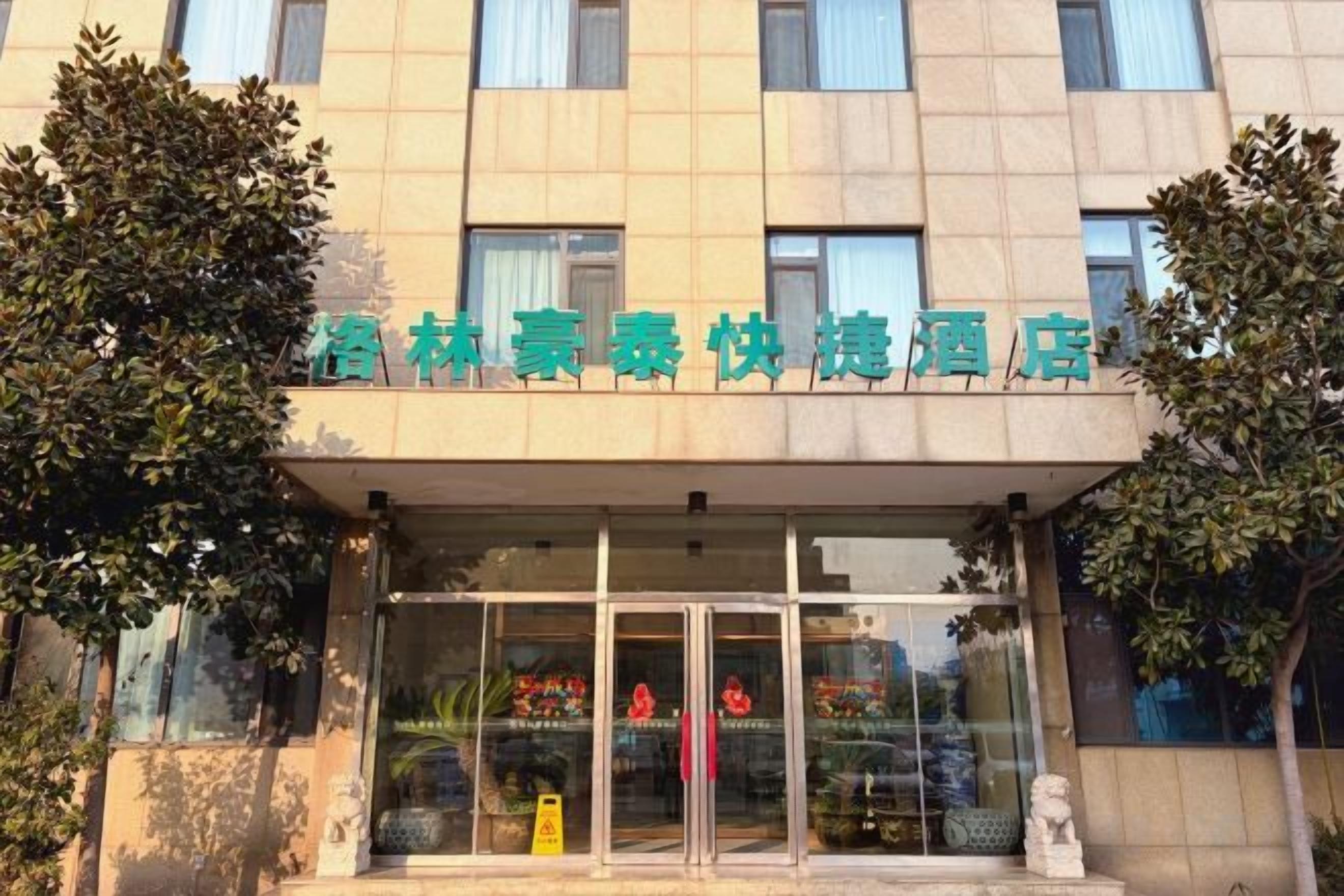 A hotel entrance with a clear glass facade, a sign above the entrance, and a statue at the base.