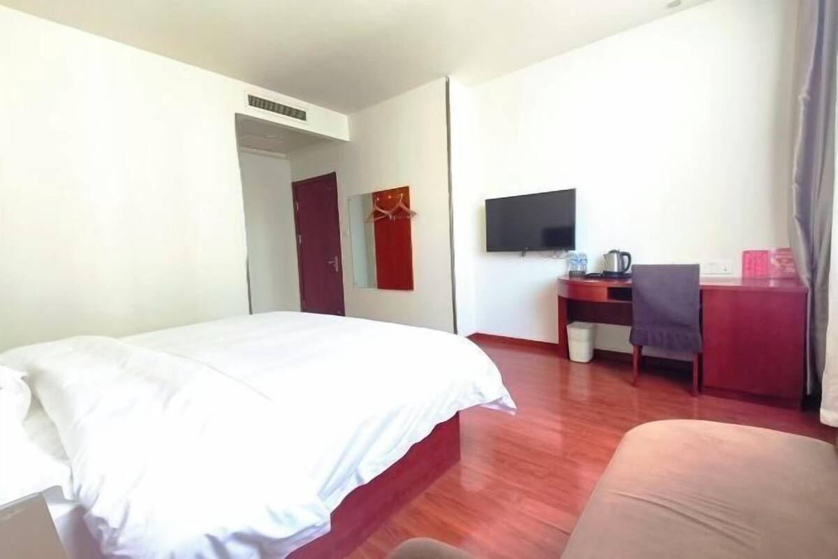 A hotel room with a bed, a desk with a chair, a television, and a small table with a kettle.