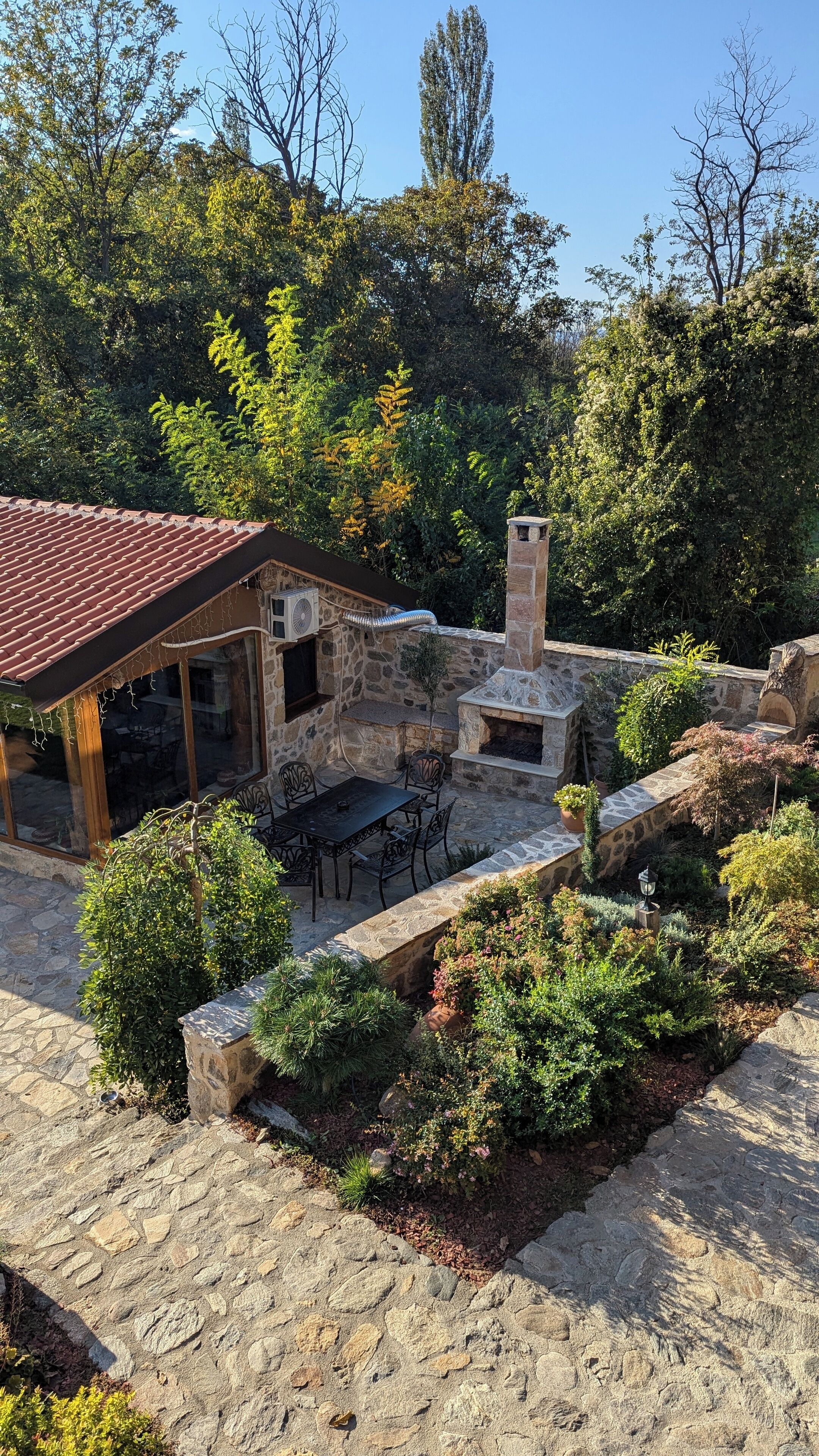 Une terrasse extérieure dotée d’un sol en pierre, d’une cheminée en pierre et d’un espace salon couvert avec des tables et des chaises.