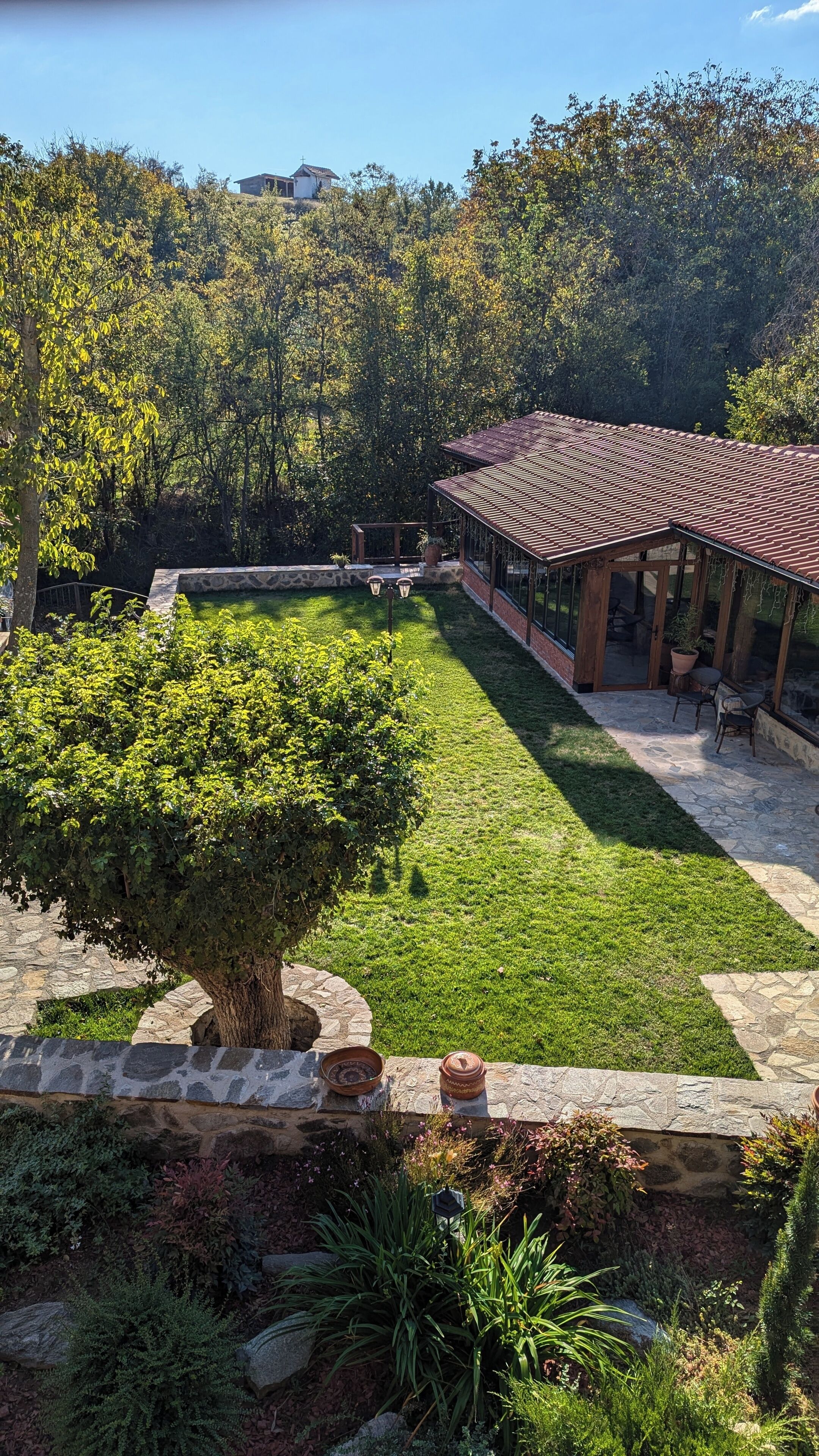 Une cour avec un mur en pierre, une pergola et un petit bâtiment doté d’un toit en tuiles.