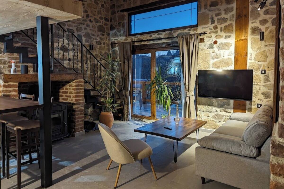 Ein gemütliches Wohnzimmer mit Steinwand, Kamin, einer Couch, einem Couchtisch und einem an der Wand montierten Fernseher.