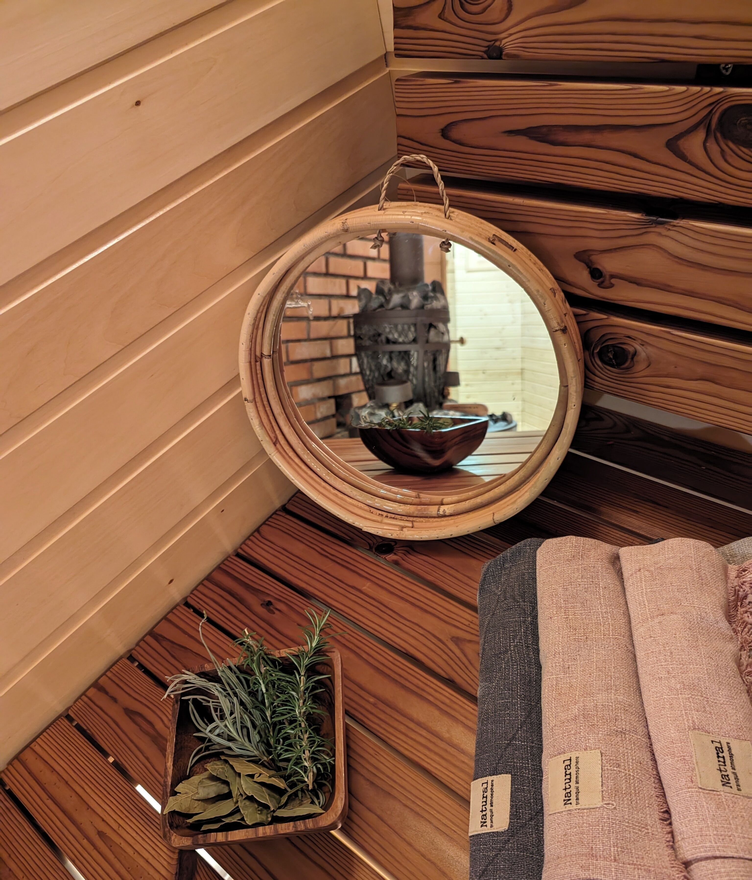 A wooden interior with a round mirror reflecting a fireplace, a bowl of herbs, and a small wooden tray with more herbs.