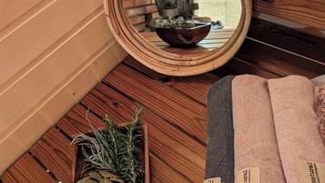 A wooden interior with a round mirror reflecting a fireplace, a bowl of herbs, and a small wooden tray with more herbs.