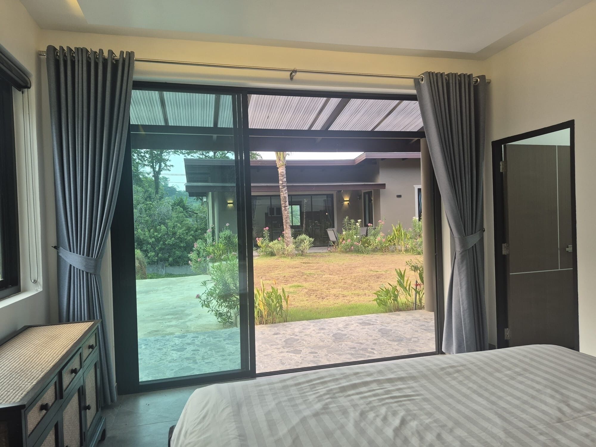 A bedroom with a large bed, a view of a garden, and a sliding glass door leading outside.