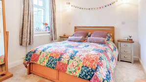 A bedroom with a wooden bed, floral bedding, a window with curtains, a bedside table with a clock, and a wall-mounted light fixture. - 1 bedroom accommodation in Durham (Durham)