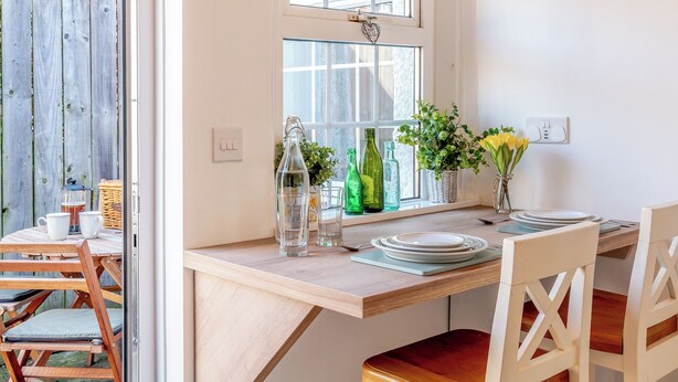 A wooden dining table with chairs, a window with a view, and various items on the windowsill including bottles and a plant. - 1 bedroom accommodation in Durham (Durham)