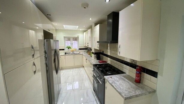 A modern kitchen with white cabinets, a stainless steel refrigerator, a gas stove, and a fire extinguisher. - Tooting Stays (London)