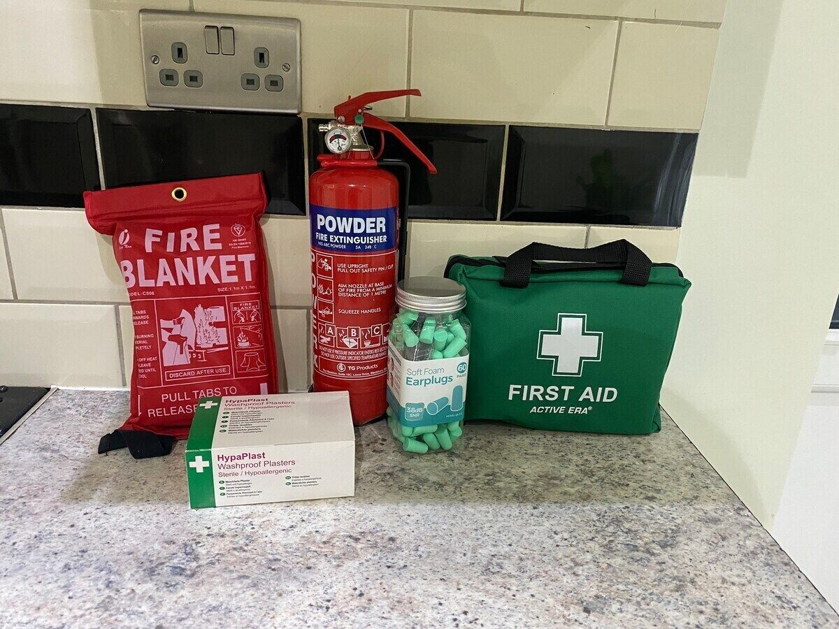 Eine Küchenarbeitsplatte mit einer Feuerdecke, einem Pulverlöscher, einem Erste-Hilfe-Set und einer Packung Ohrstöpsel.
