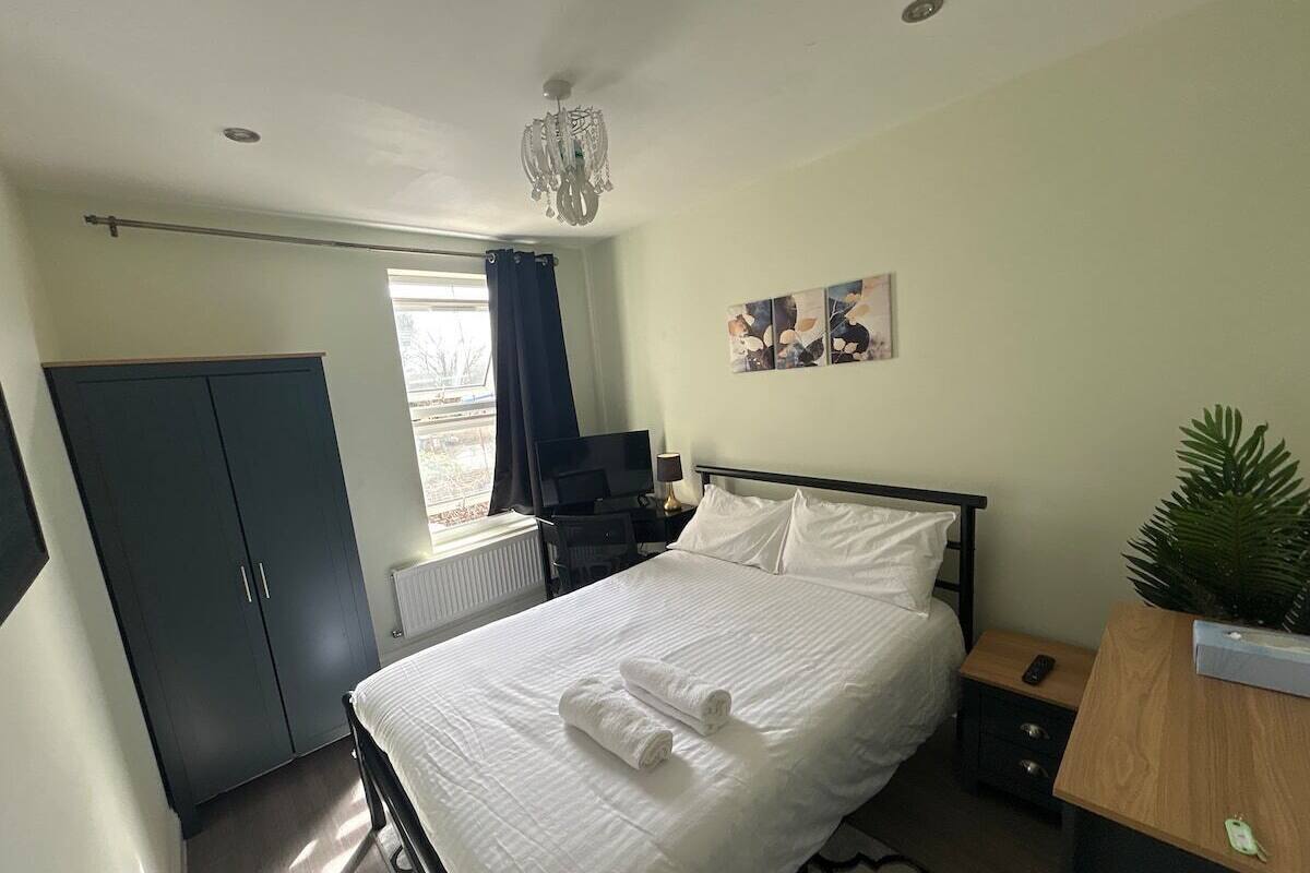 A bedroom with a bed, a desk, a wardrobe, a television, and a window with curtains.