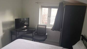 Habitació d'hotel amb llit, escriptori amb televisió, cadira i finestra amb cortines.