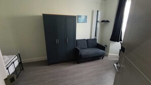 A room with a dark blue wardrobe, a grey sofa, and a window with curtains. - Tooting Stays (London)