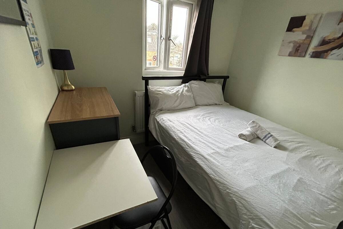 A small, tidy room with a single bed, a desk, and a chair.