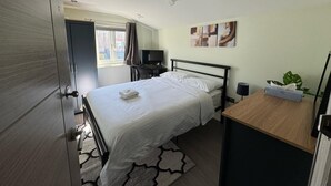A hotel room with a bed, a desk, a TV, and a window with curtains. - Tooting Stays (London)