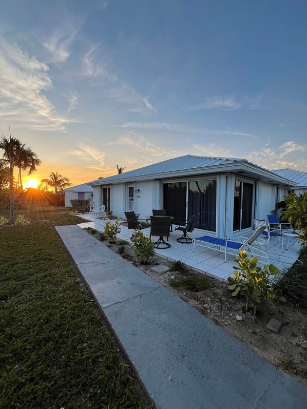 A single-story house with a covered patio area, a small garden, and a clear view of the sunset.