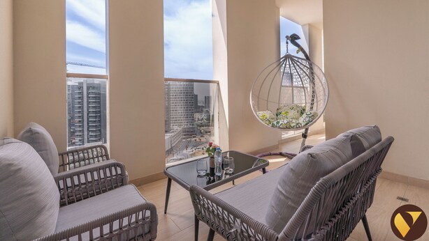 A balcony with wicker furniture, a hanging chair, and a table with glasses and a bottle. - Vogue | Canal Bay close to Burj Khalifa Dubai Mall (Dubai)