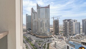A high-rise building with a curved facade, surrounded by other modern buildings and a busy road with greenery. - Vogue | Canal Bay close to Burj Khalifa Dubai Mall (Dubai)