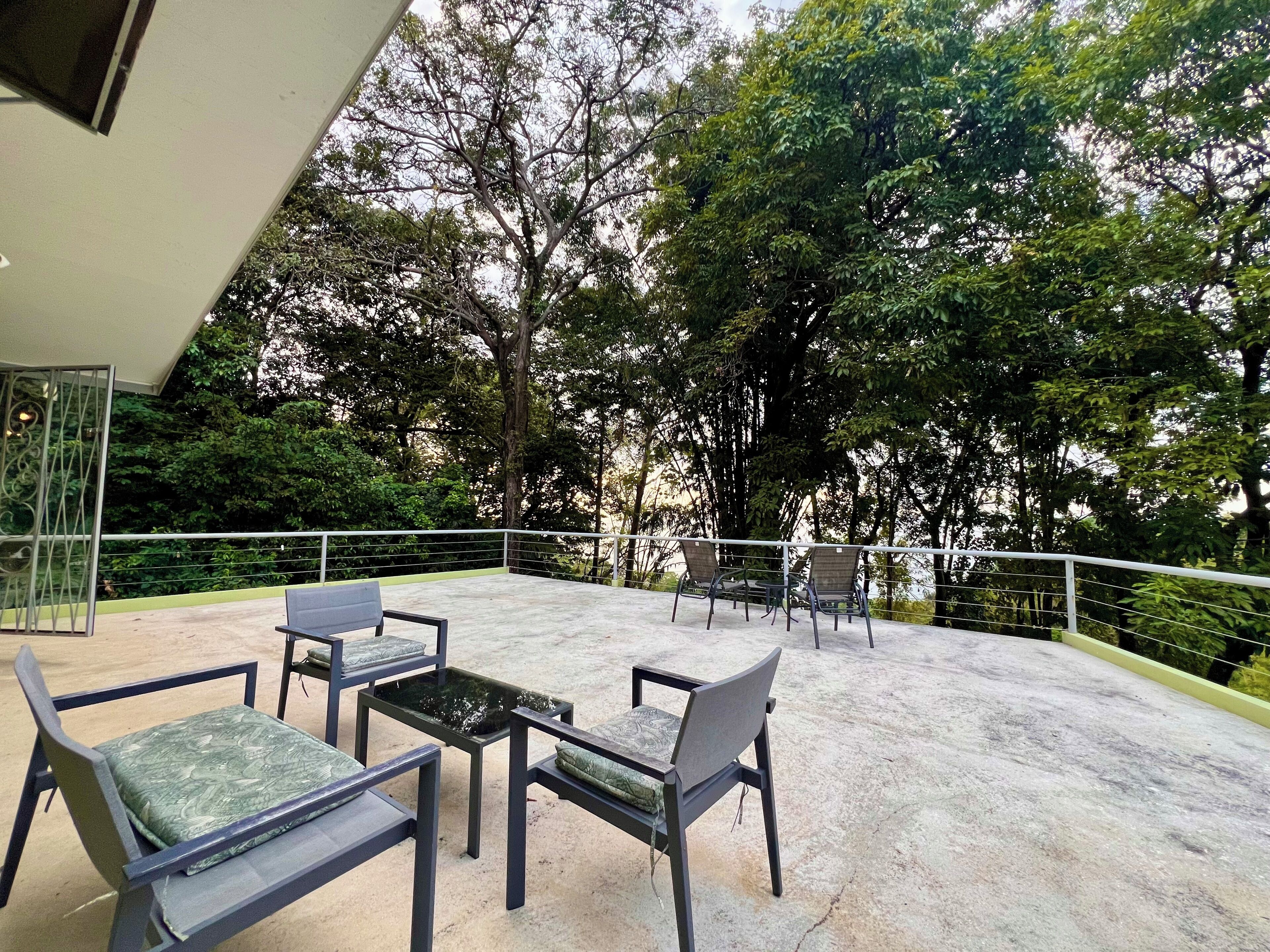 An outdoor seating area with a concrete floor, surrounded by a metal railing, and overlooking a lush green landscape.