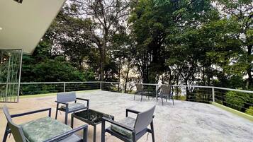 An outdoor seating area with a concrete floor, surrounded by a metal railing, and overlooking a lush green landscape.