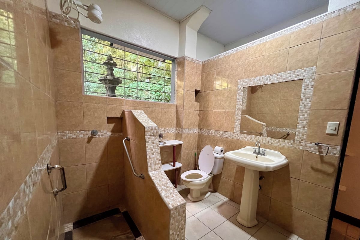 A bathroom with a shower, toilet, and sink, featuring tiled walls and a window with a view of greenery.