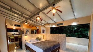 A modern bedroom with a large bed, a ceiling fan, and a view of the outdoors through a large window. - Zen Zaru Beautiful Hidden Hotel (Quepos)