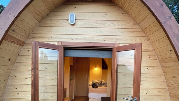 Una struttura in legno ad arco con una porta che dà su una stanza con un letto e una panca.