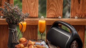 Un tavolo in legno con articoli per la colazione, un altoparlante e un vaso con fiori.