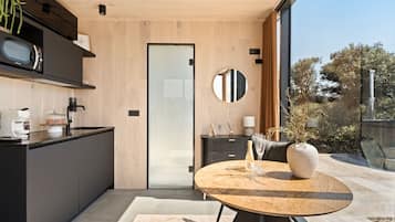 Una cocina moderna con encimera de madera, microondas integrado y puerta de vidrio que da a un comedor con una mesa redonda y sillas.