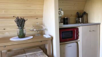 A compact kitchenette with a red microwave, a small refrigerator, and a wooden table with a vase of lavender.