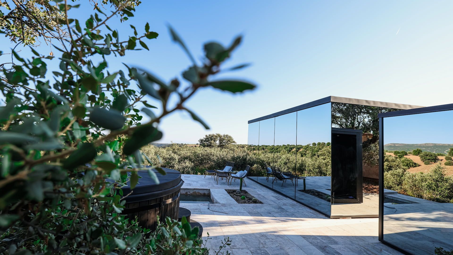 A modern outdoor patio with seating, a glass door leading to a private area, and a view of a vineyard.