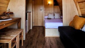 Un interno accogliente in legno, con soffitto a volta, un letto, una scrivania e un angolo cottura.