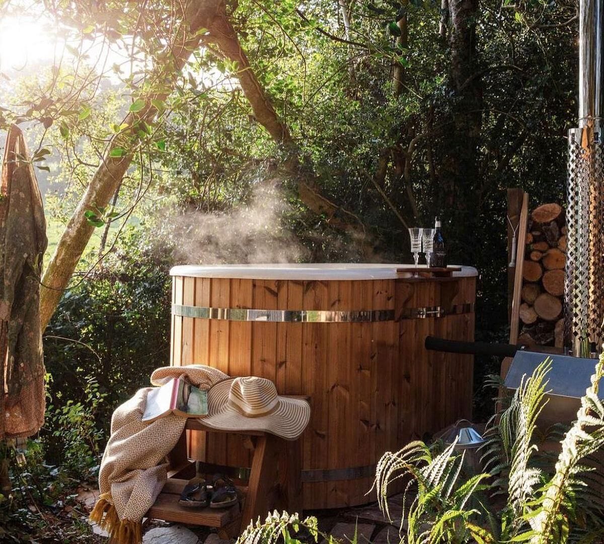 Ein Whirlpool inmitten von Bäumen mit einer Holzterrasse, einem Hut und einer Decke.