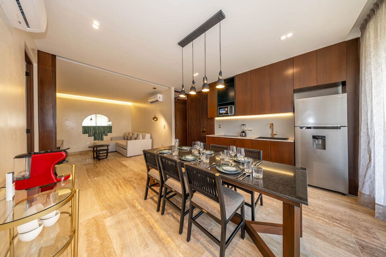 A modern kitchen with wooden cabinets, a stainless steel refrigerator, and a dining area with a glass table and chairs.