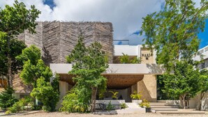 A modern building with a unique zigzag roof design, surrounded by lush greenery and a gravel courtyard. - Lux 2BR w/ Rooftop Pool+ Close to Beach (Tulum)