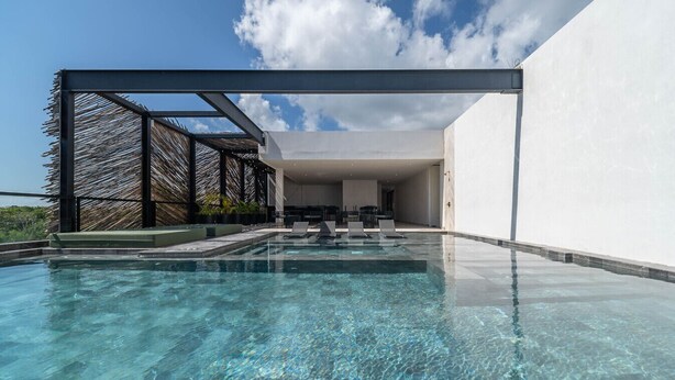 A modern outdoor swimming pool with clear water, surrounded by a minimalist architectural design and a thatched structure. - Lux 2BR w/ Rooftop Pool+ Close to Beach (Tulum)