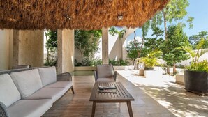An outdoor seating area with a thatched roof, cushioned sofas, and a wooden table. - Lux 2BR w/ Rooftop Pool+ Close to Beach (Tulum)