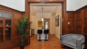 A hallway with wooden paneling, a potted plant, a bar area with stools, and a patterned armchair.