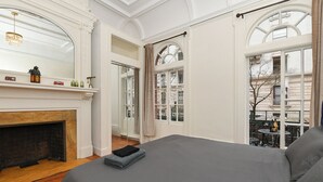 A bedroom with a large bed, a fireplace, and large windows with curtains.
